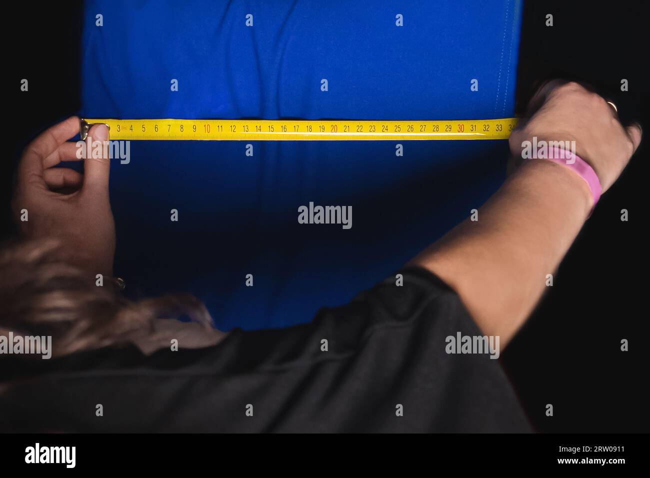 Le mani di una sarta professionista misurano le dimensioni di un tessuto vintage blu per lavorare con abiti con un righello, un metro a nastro. Foto Stock