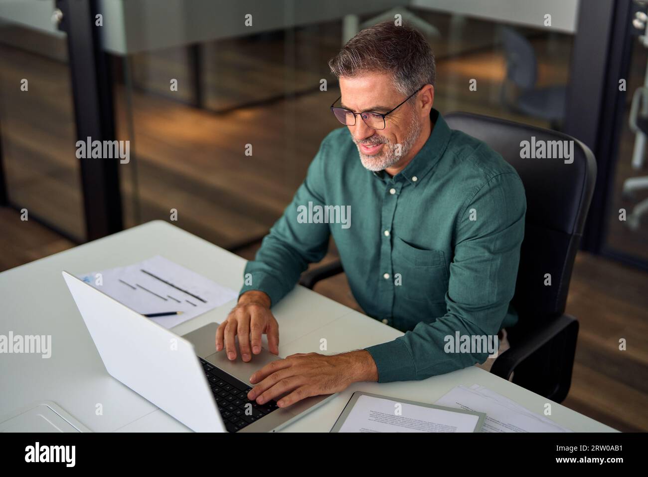 Uomo d'affari professionale sorridente e impegnato di mezza età che lavora con un notebook in ufficio. Foto Stock