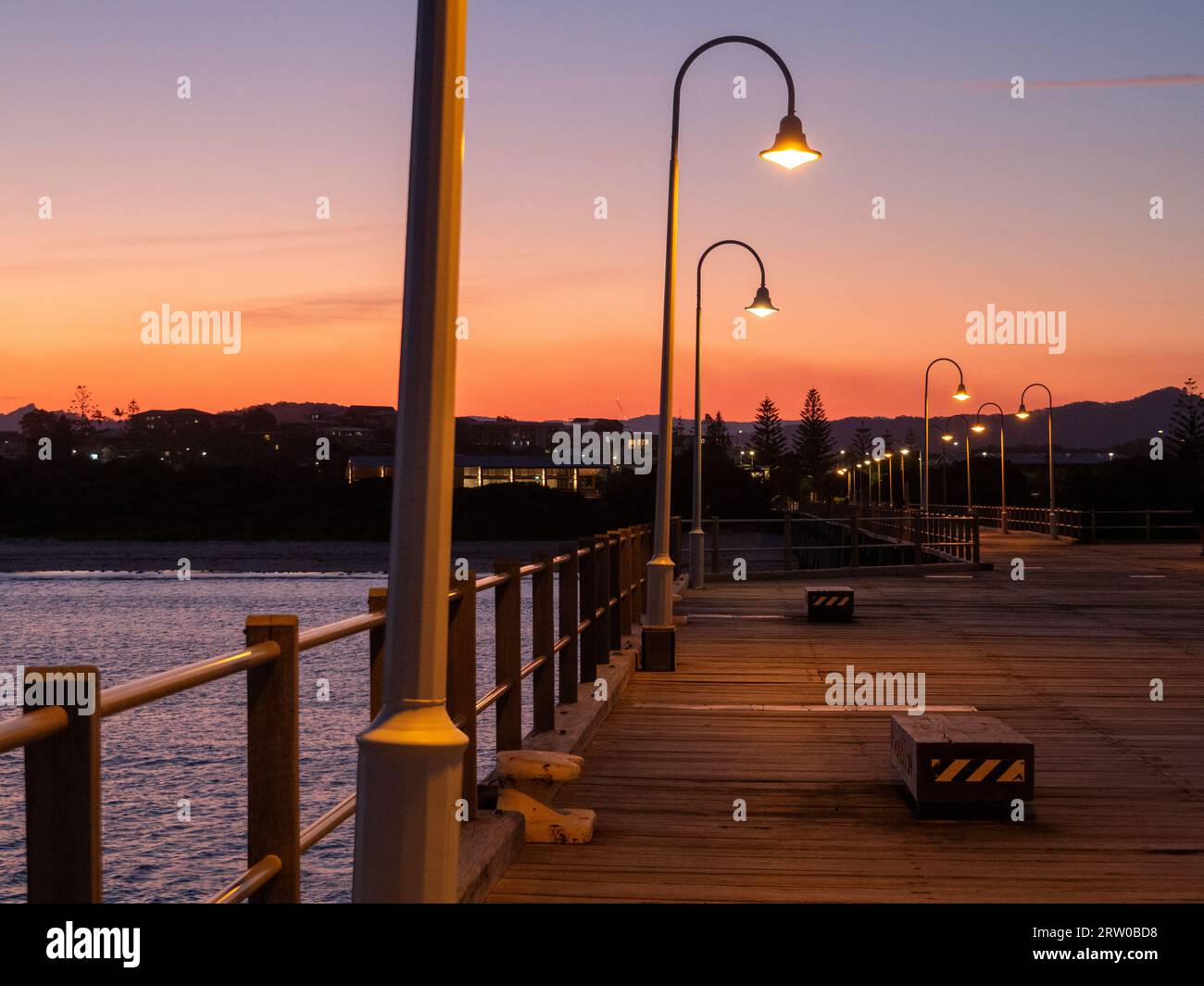 Cielo arancione, molo di Coffs Harbour al tramonto, alberi curvi accesi Foto Stock