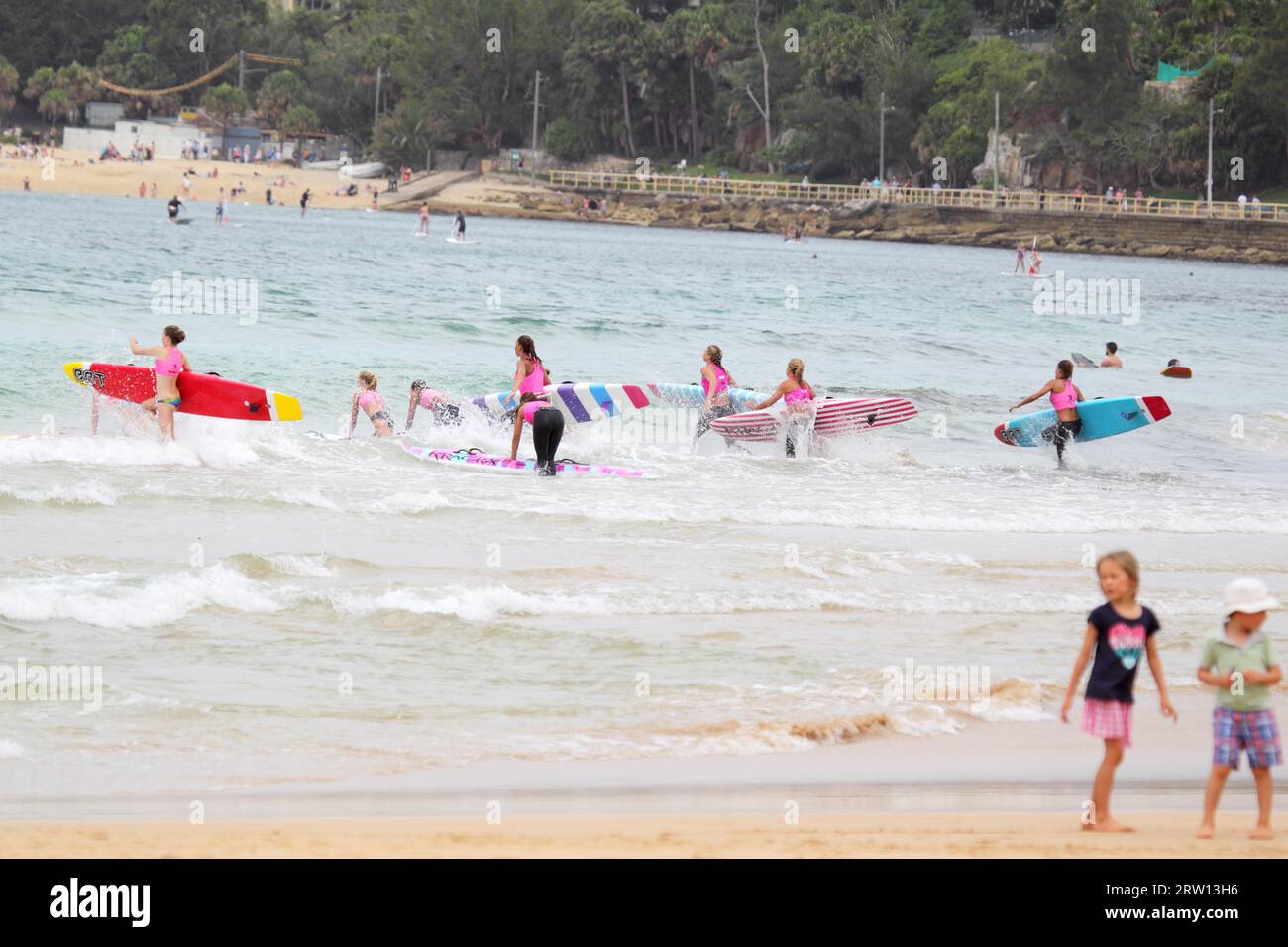 Gli studenti di una scuola di surf corrono con le loro tavole da surf in mare a Manly Beach, Sydney, Australia Foto Stock
