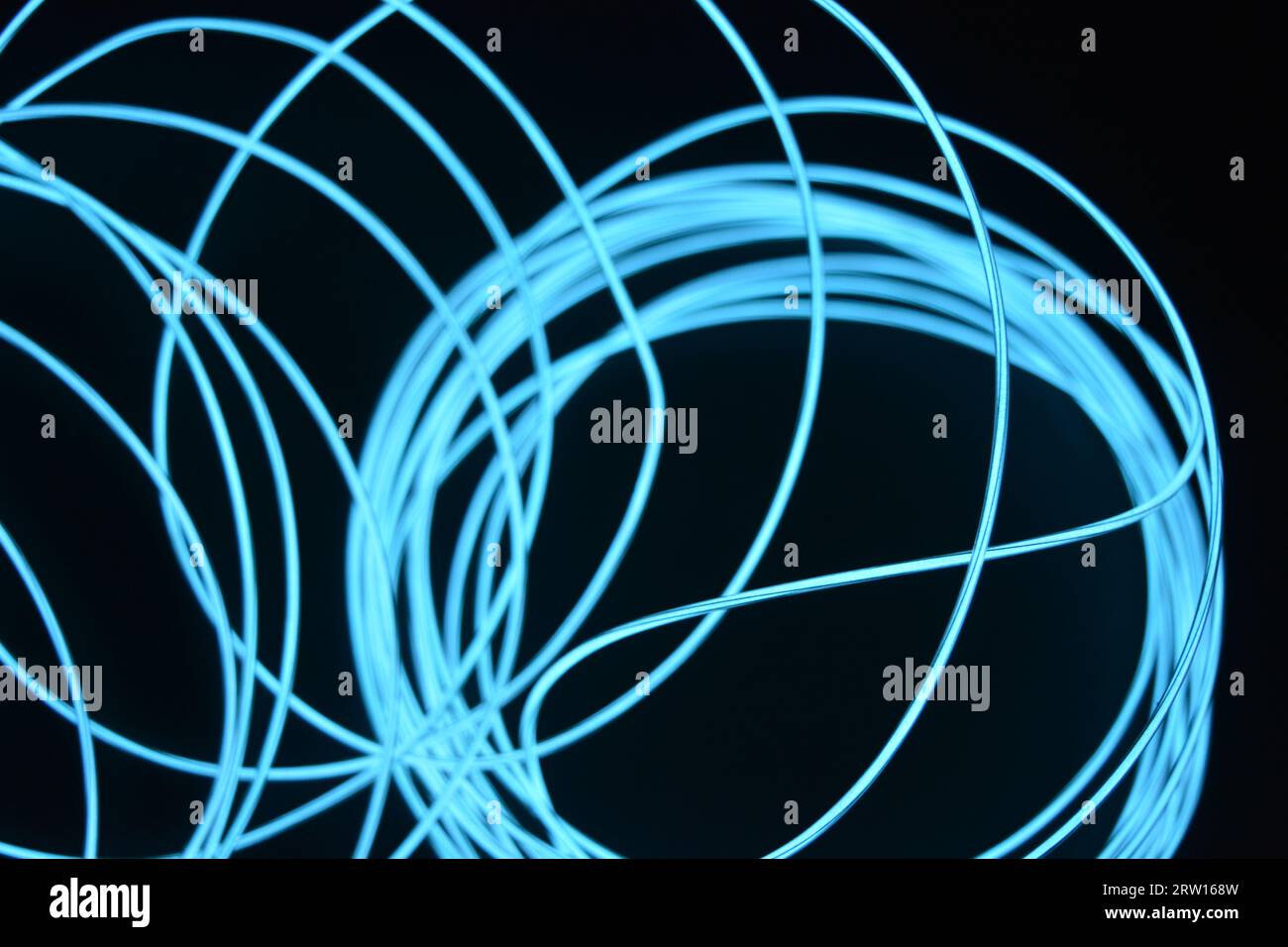 Uno sfondo insolito, unico e luminoso di cavi sottili impilati in modo caotico, celeste, blu, azzurro, imbracatura al neon, filo illuminato, filo sottile posizionato Foto Stock