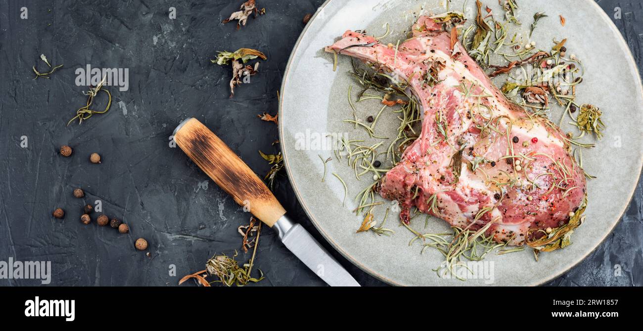 Bistecca di maiale cruda Tomahawk marinata con erbe speziate su fondo di pietra. Copia spazio. Foto Stock