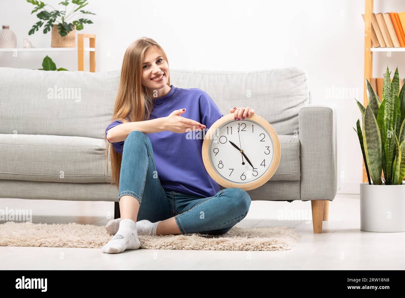 Bella ragazza con un grande orologio sul divano, concetto di orario di lavoro. Foto di alta qualità Foto Stock