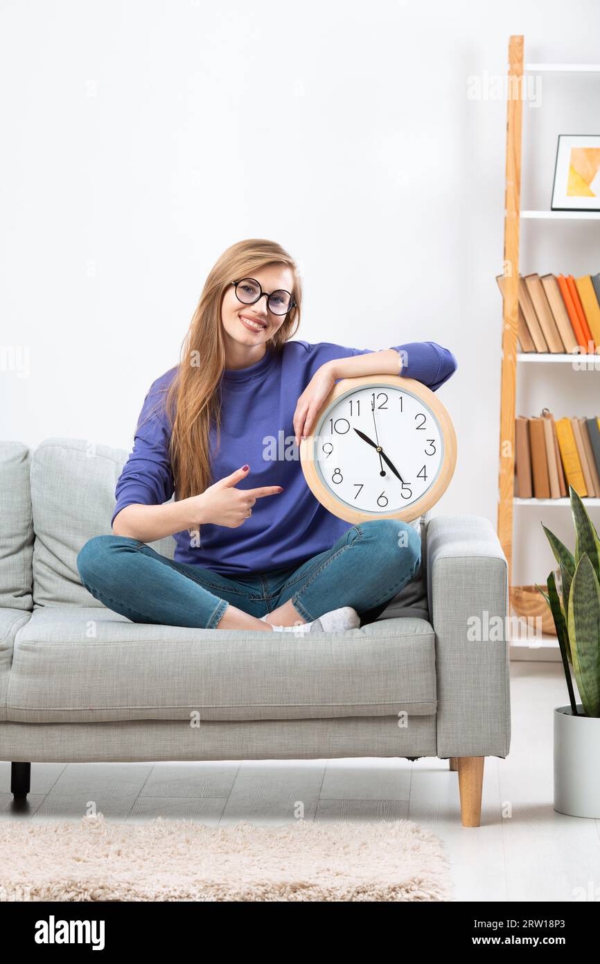 Bella ragazza con un grande orologio sul divano, concetto di orario di lavoro. Foto di alta qualità Foto Stock