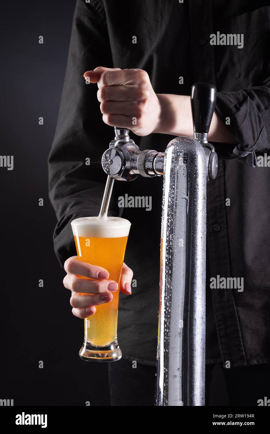 Il barista versa birra fresca dal rubinetto in un bicchiere su sfondo scuro. Foto di alta qualità Foto Stock