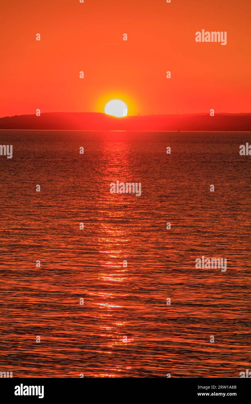 Una striscia di luce solare che attraversa il canale di Bristol al tramonto con un bagliore di arangee rossiccio Foto Stock