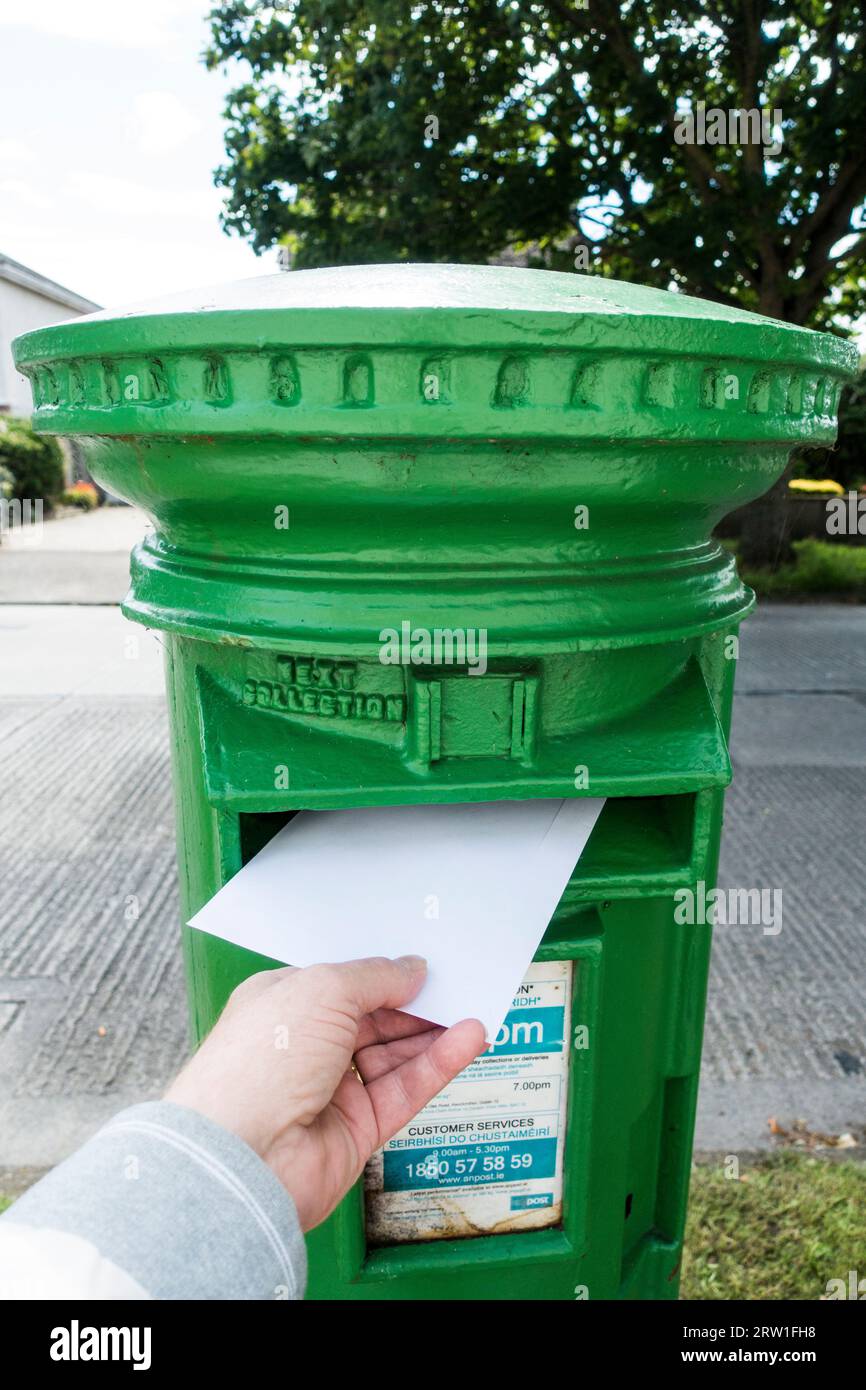 Mano Mans che spedisce una lettera in una cassetta postale irlandese Foto Stock