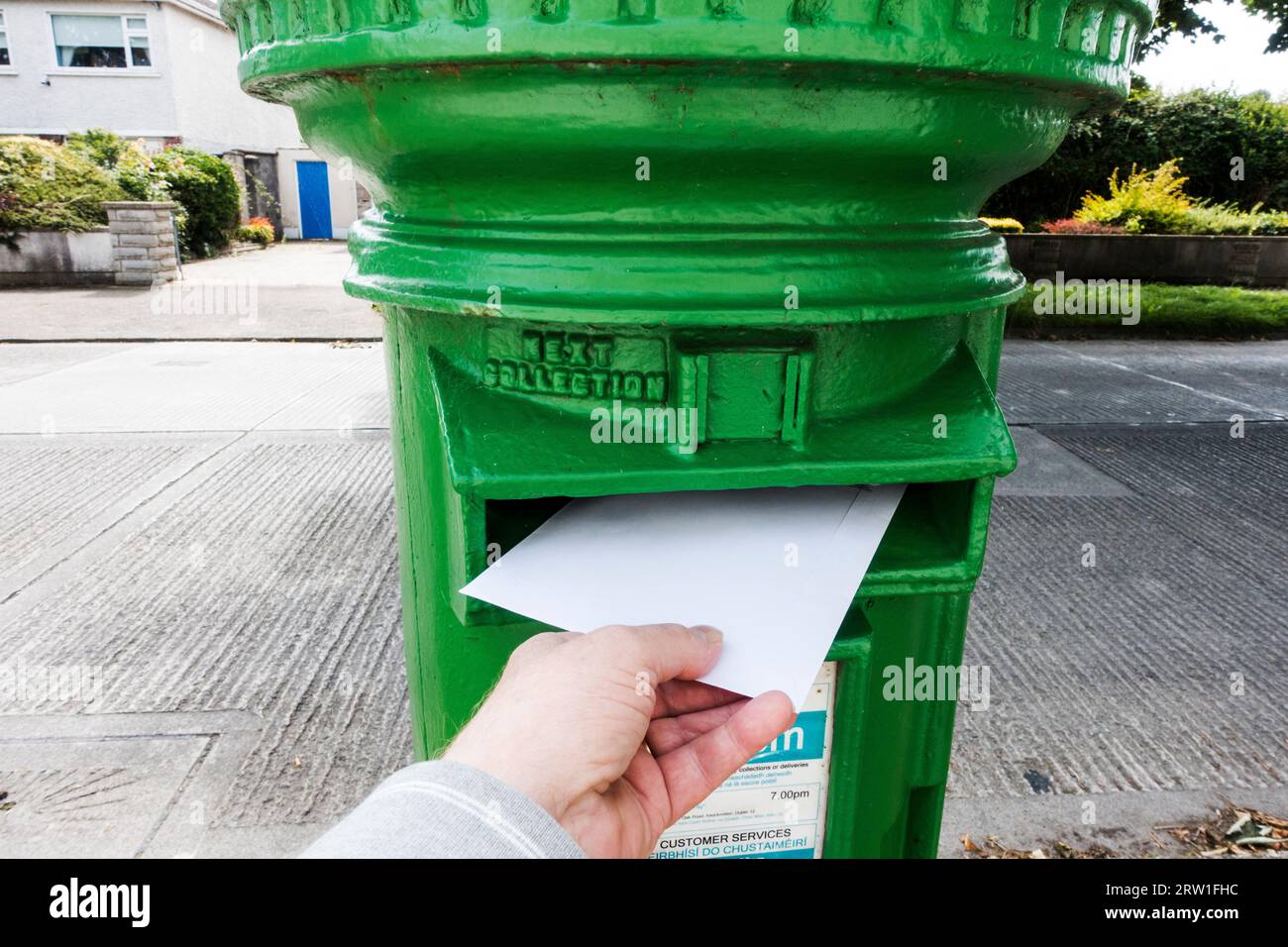 Mano Mans che spedisce una lettera in una cassetta postale irlandese Foto Stock