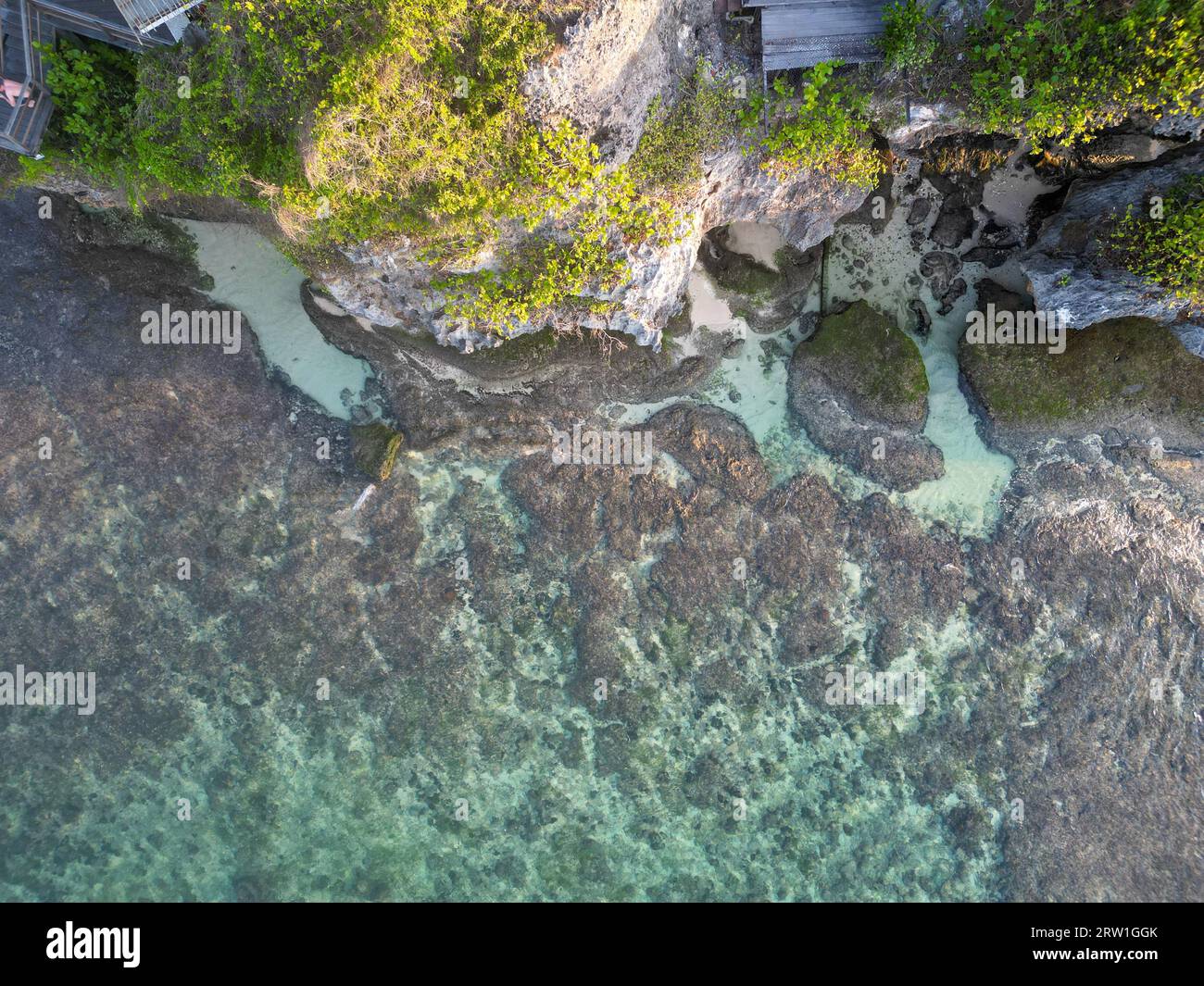 Vista aerea dall'alto verso il basso di acque cristalline con onde che si infrangono contro le rocce di Bali Foto Stock