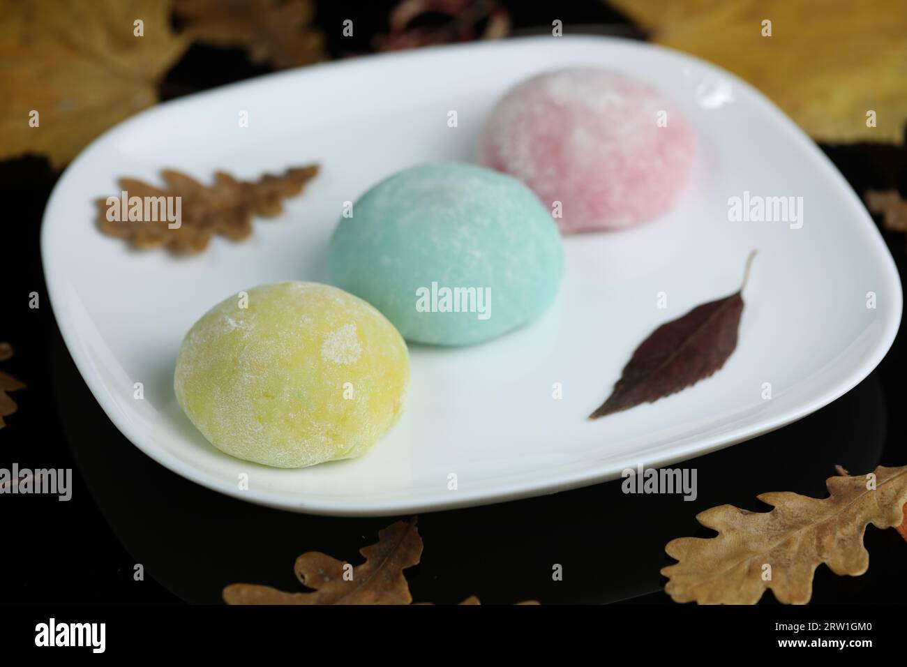 Dolci giapponesi colorati daifuku o mochi. I dolci si avvicinano al piatto  con lo sfondo delle foglie autunnali e le candele Foto stock - Alamy