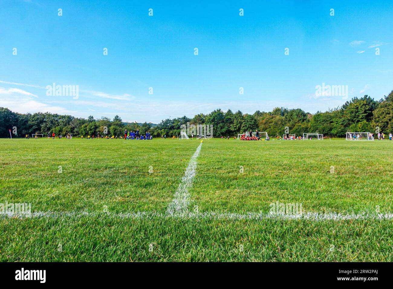 Squadre di calcio giovanili che giocano nel parco il sabato mattina con un campo verde e un cielo blu Foto Stock