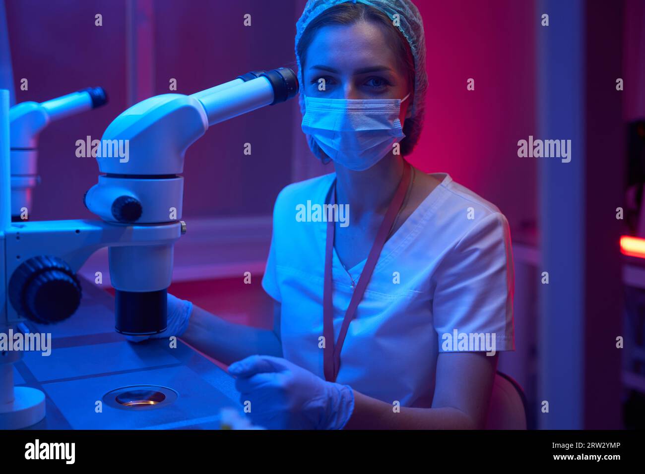 L'assistente di laboratorio in una maschera protettiva utilizza un microscopio potente Foto Stock