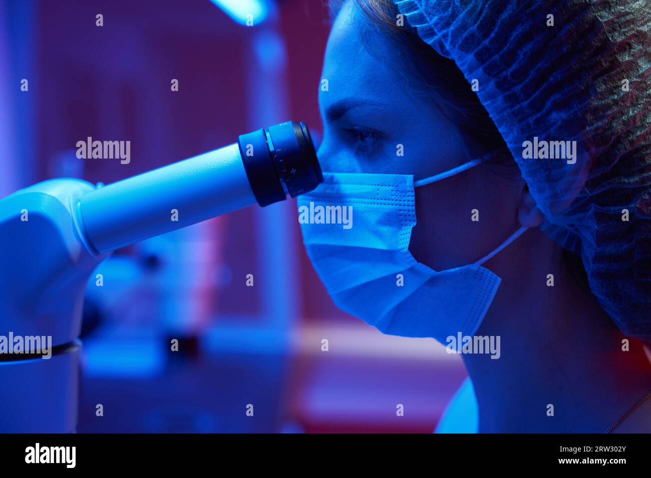 Donna in uniforme medica guarda attraverso un potente oculare microscopio Foto Stock