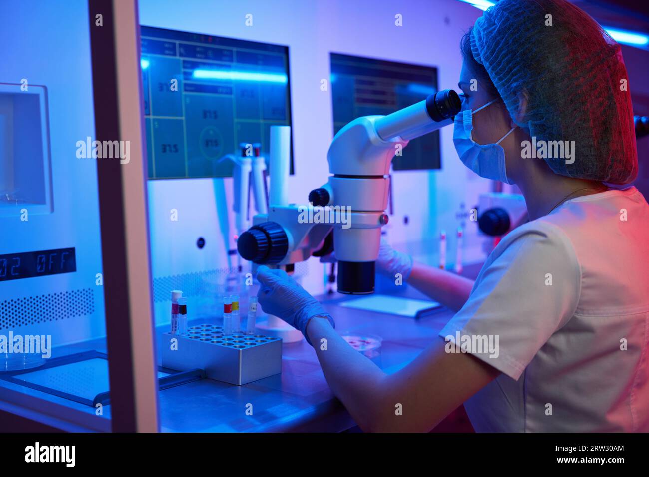 L'assistente di laboratorio utilizza un microscopio potente nel suo lavoro Foto Stock