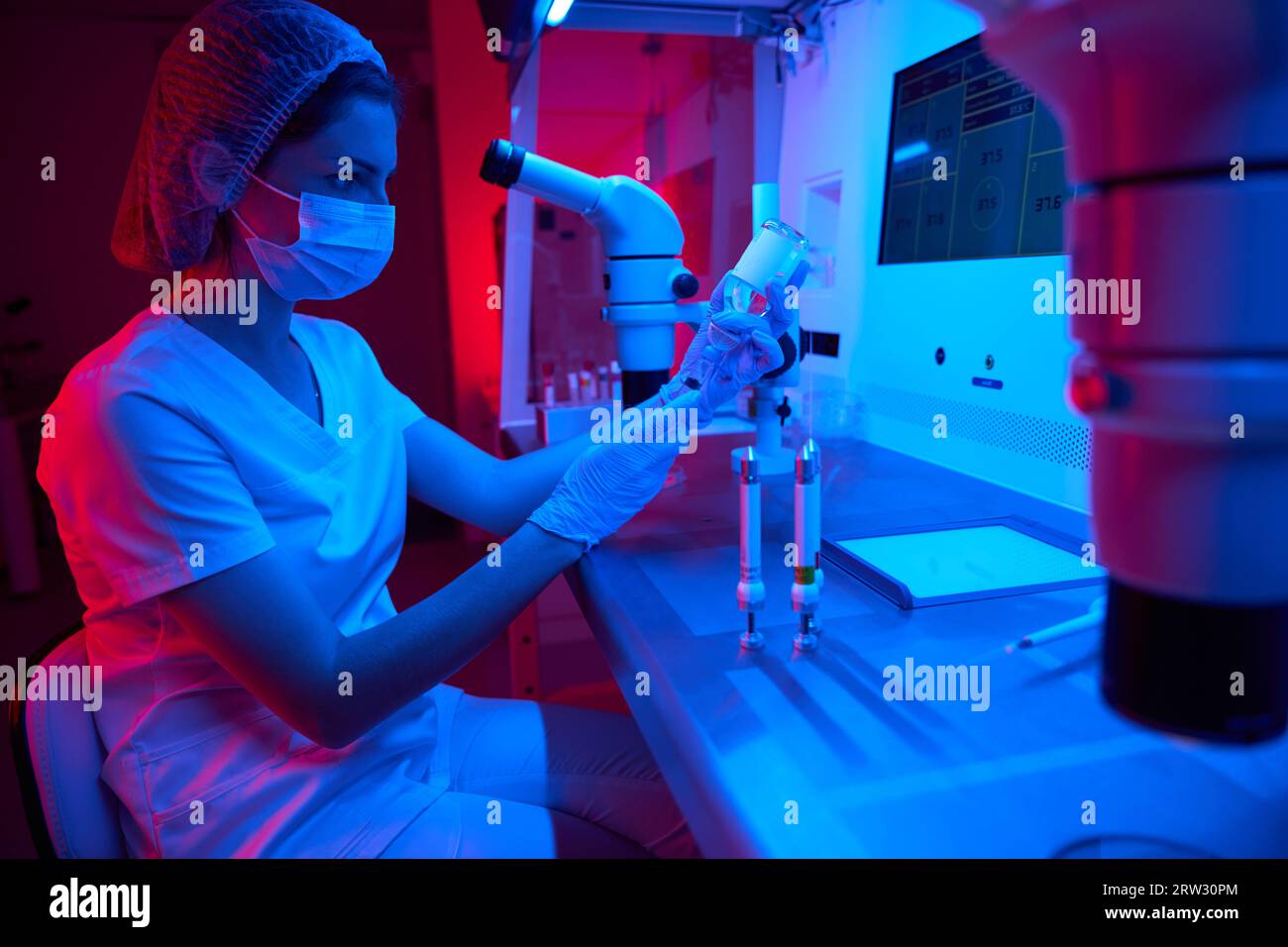 Assistente di laboratorio femminile in una maschera protettiva conduce la procedura ICSI Foto Stock
