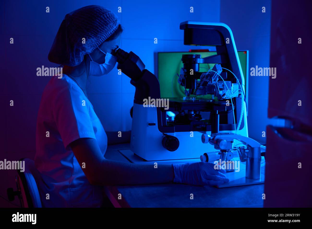 Scienziato embriologo in maschera lavora con biomateriale al microscopio Foto Stock