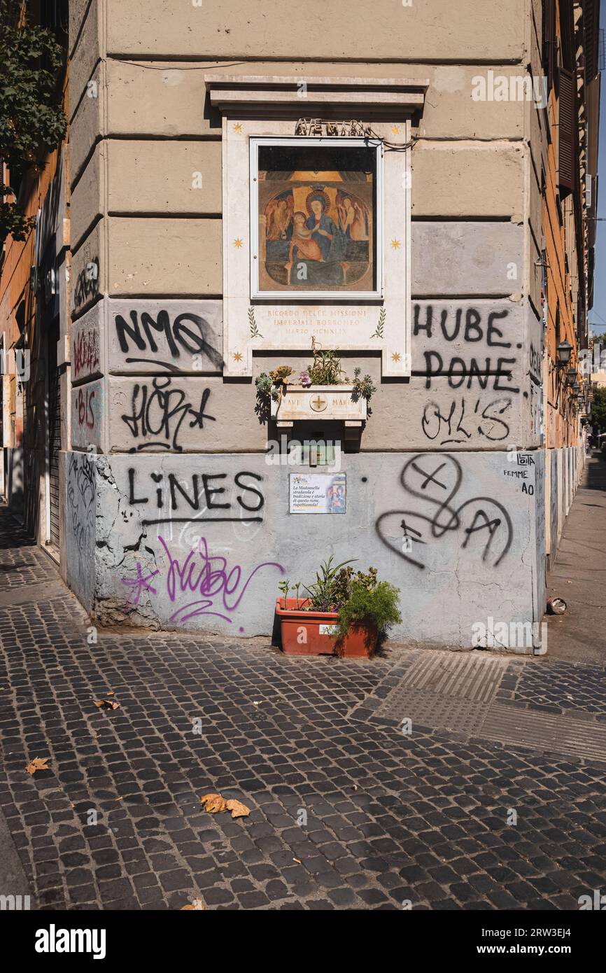 Roma, Italia - 27 agosto 2023: Graffiti urbani e vernice spray su un vecchio edificio residenziale giustappone un'opera d'arte religiosa storica di a ma Foto Stock