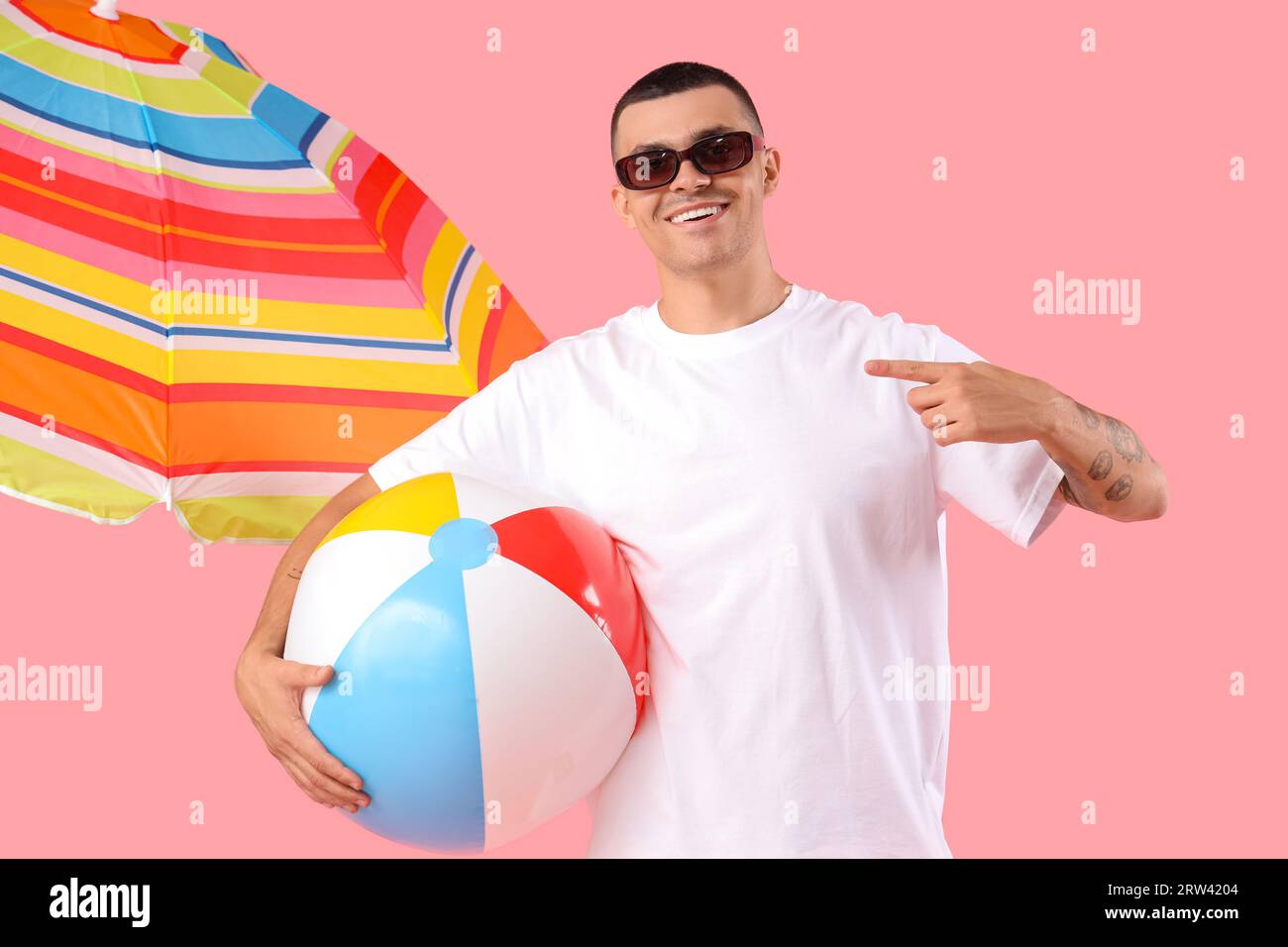 Giovane uomo felice con un ombrello che punta alla palla gonfiabile su  sfondo rosa Foto stock - Alamy