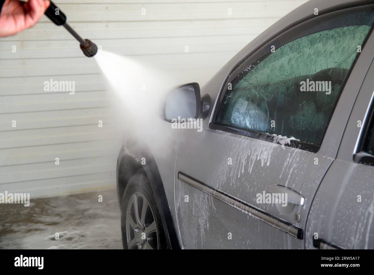 Lavaggio auto al coperto. Processo di rimozione della schiuma di sapone dal lato del veicolo con pulitrice a pressione - primo piano con messa a fuoco selettiva. Foto Stock