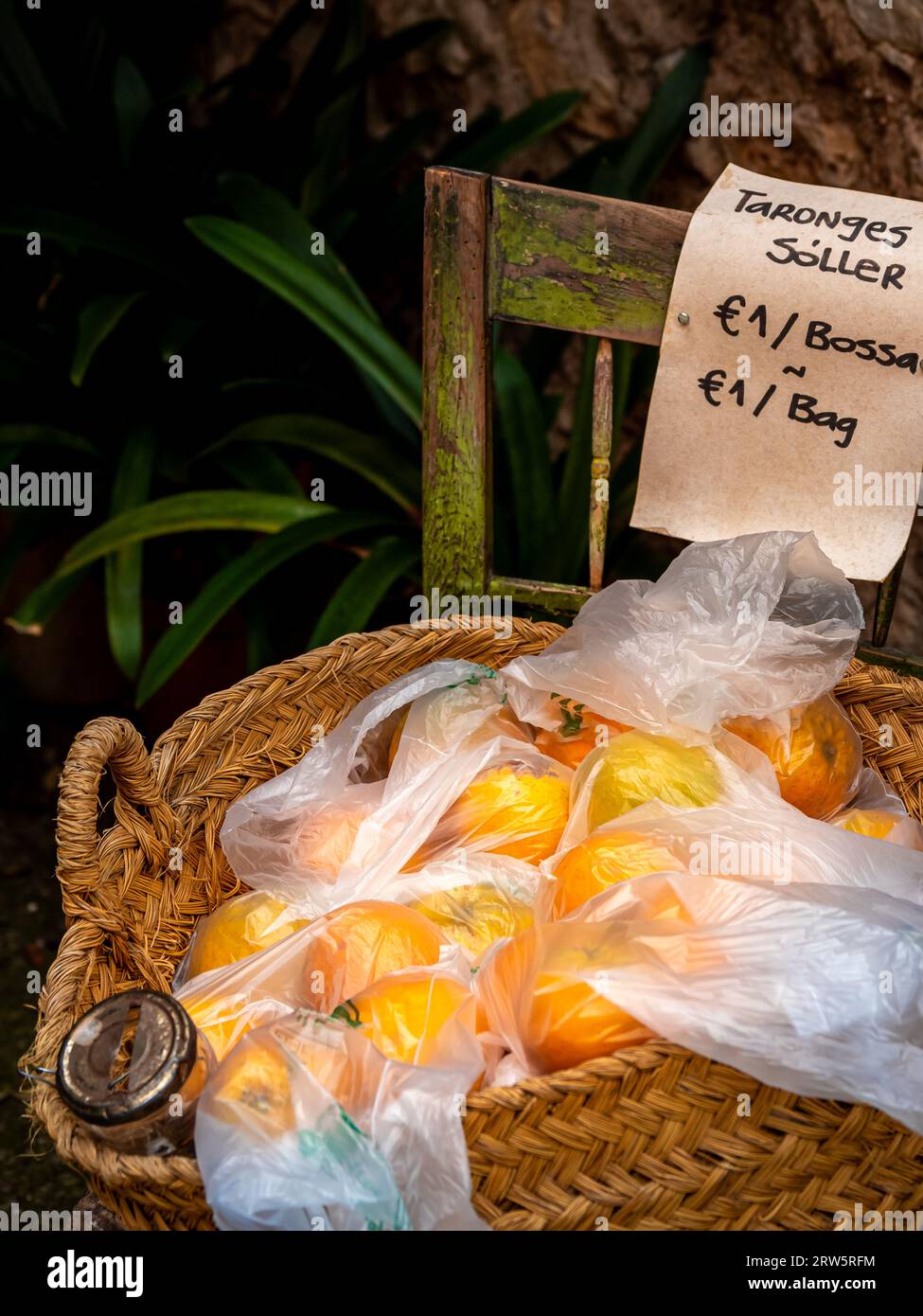 Scena del vending di strada in catalano, con le arance fresche di Sóller esposte in un cestino intrecciato su una sedia con un contenitore di monete, ogni porzione confezionata Foto Stock