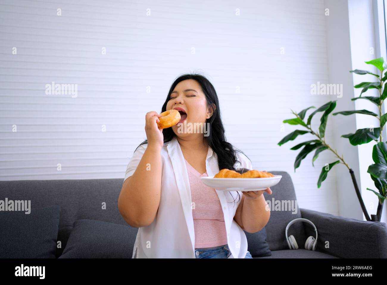 La donna Plus size sta mangiando la ciambella. Concetto di assistenza sanitaria e stile di vita. Foto Stock