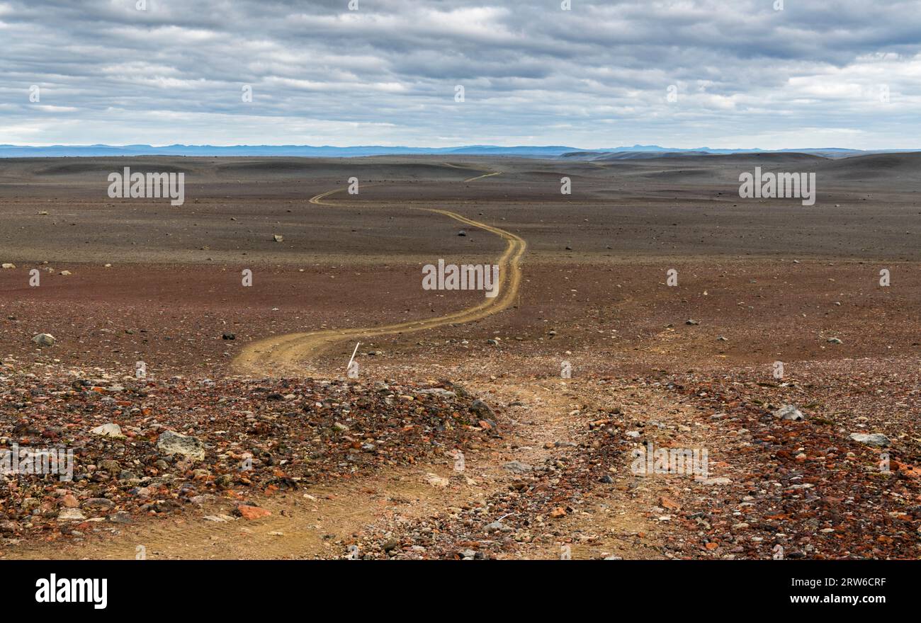 Strada tortuosa attraverso un paesaggio vulcanico solitario verso le montagne all'orizzonte, l'Islanda Foto Stock
