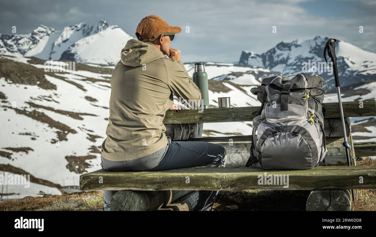 Turista caucasico che fa una breve pausa su una panchina di legno per godersi il paesaggio panoramico norvegese Foto Stock