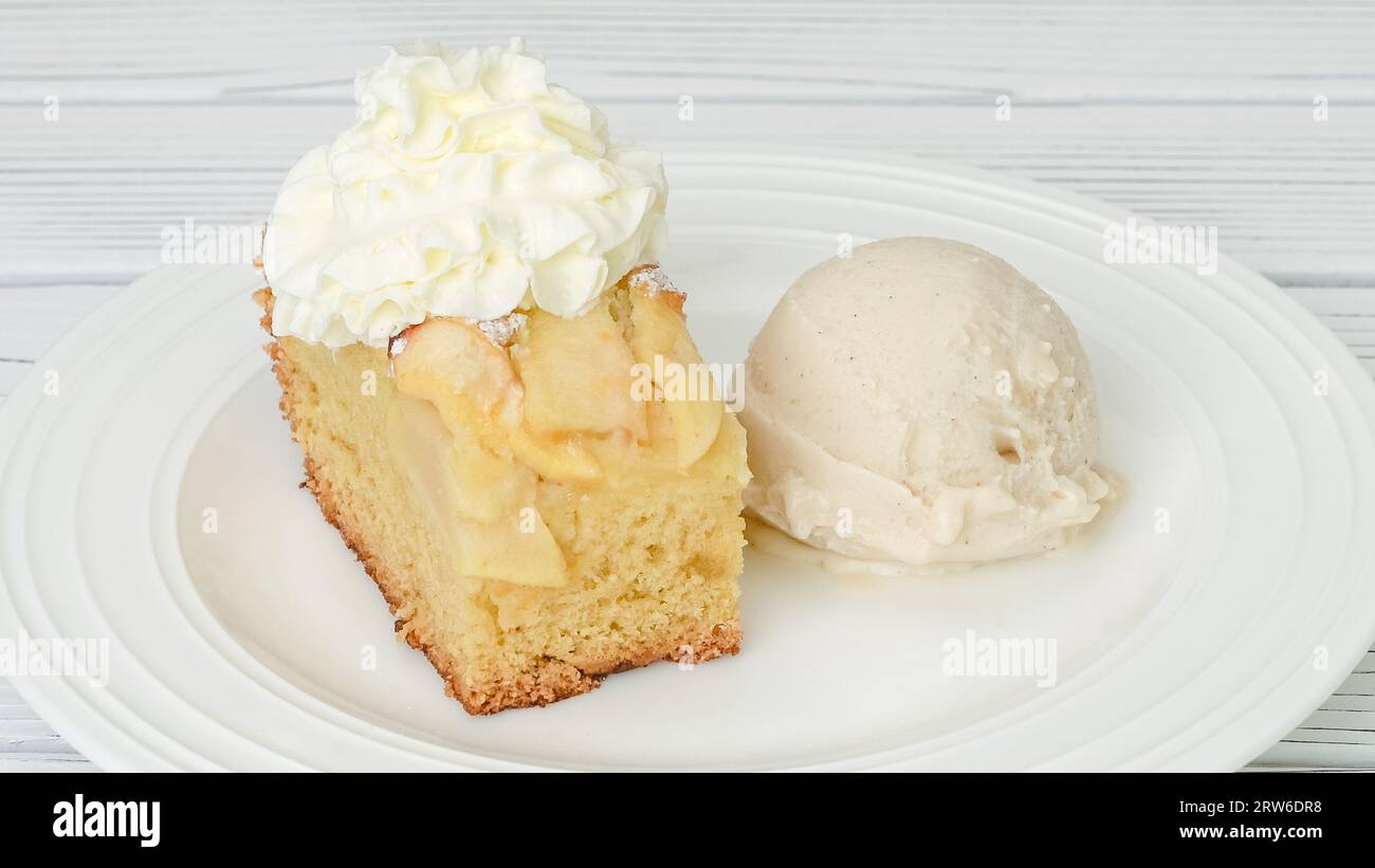 Fetta di torta di mele appena sfornata con biscotto base e mele affettate e panna montata condita con gelato alla vaniglia da vicino su un piatto su un piatto Foto Stock