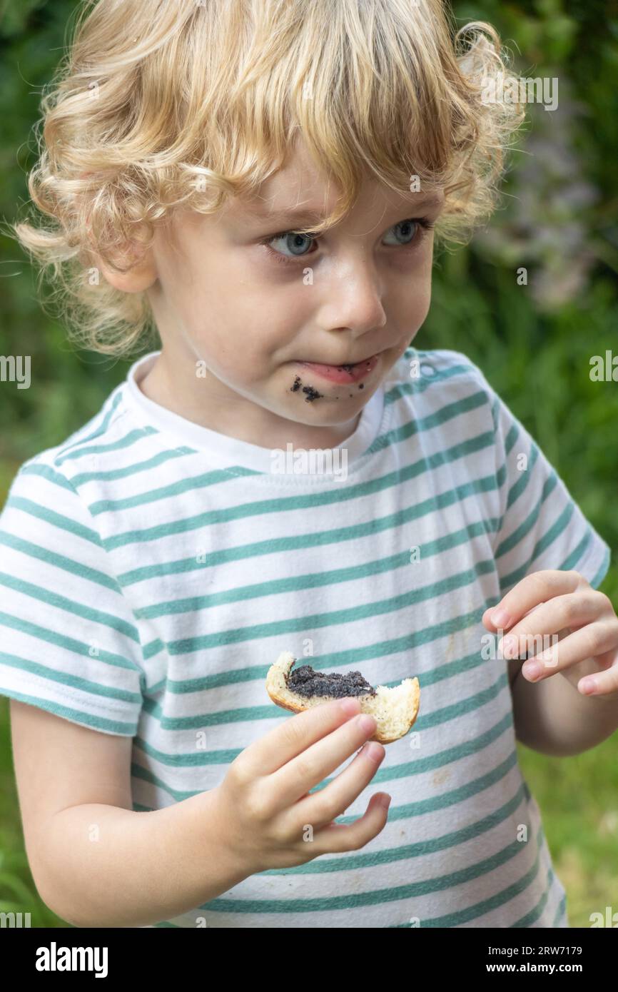 Un bambino mangia una pasticceria in un giardino Foto Stock