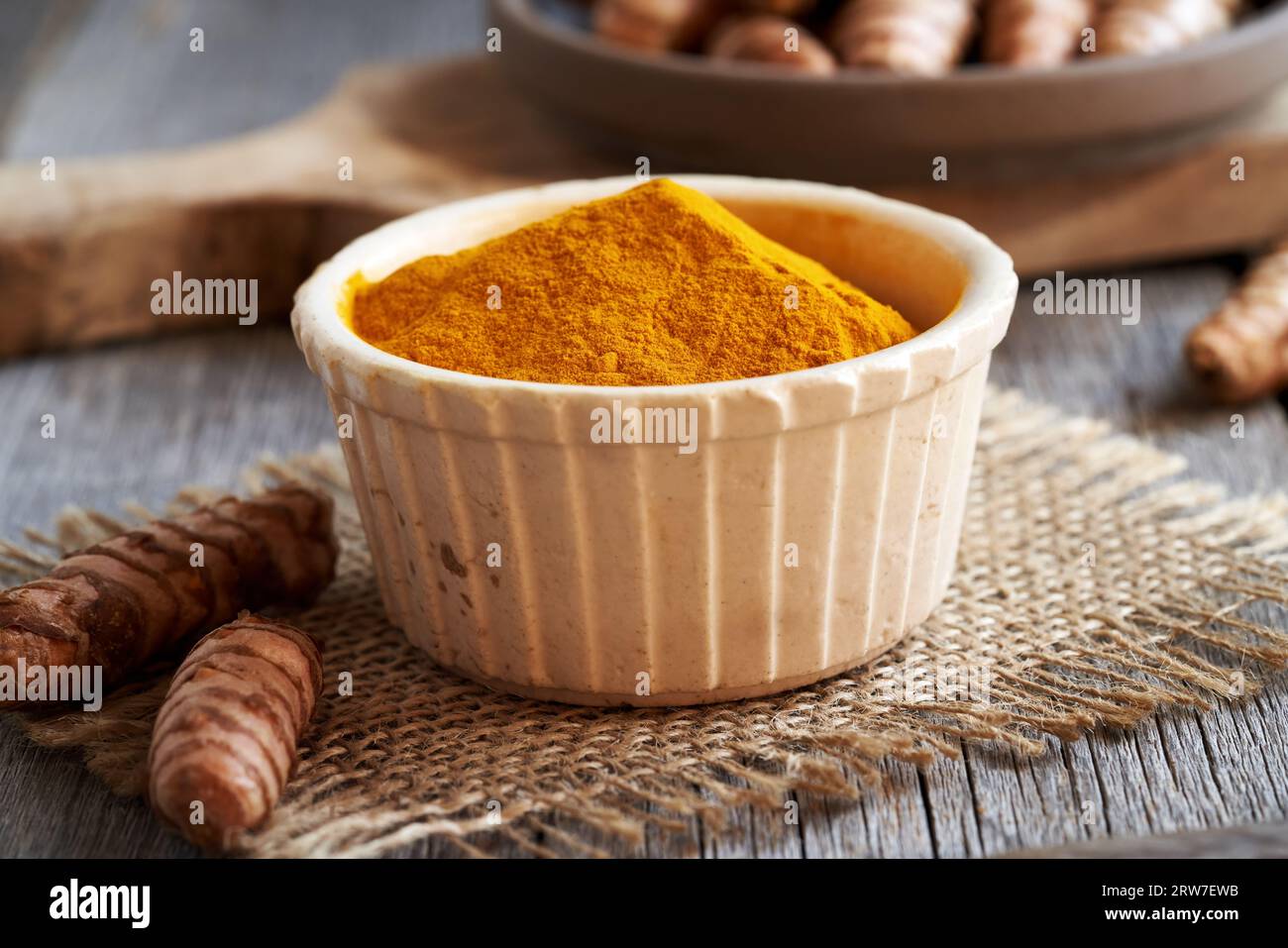 Curcuma in polvere d'arancia in un recipiente di ceramica, con radice fresca Foto Stock