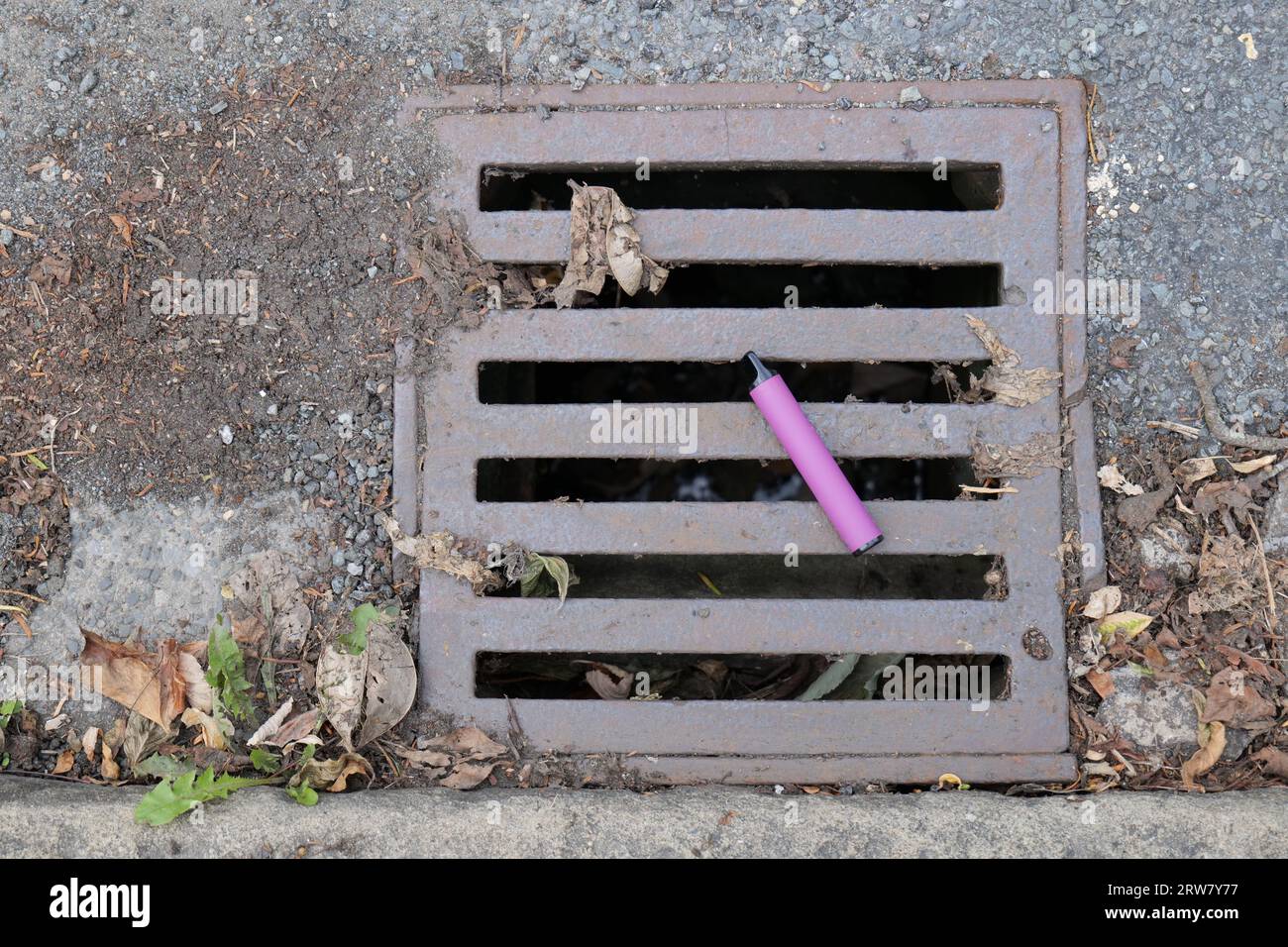 Uno svapo viola per sigaretta elettronica è stato gettato e lasciato sdraiato su un coperchio metallico dello scarico dell'acqua. Foto Stock