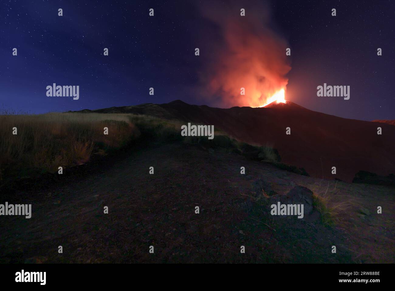 Etna - suggestiva eruzione con luci soffuse durante un'esplosione di lava nel cratere con emissione di cenere e con il cielo stellato sullo sfondo Foto Stock