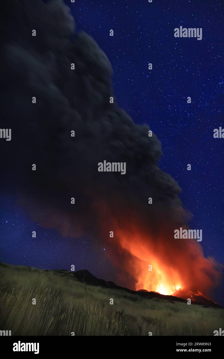 Etna eruzione in Sicilia con vista panoramica della grande colonna di fumo e cenere dal cratere vulcano nel ciel notturno stellato del agosto 2023 Foto Stock