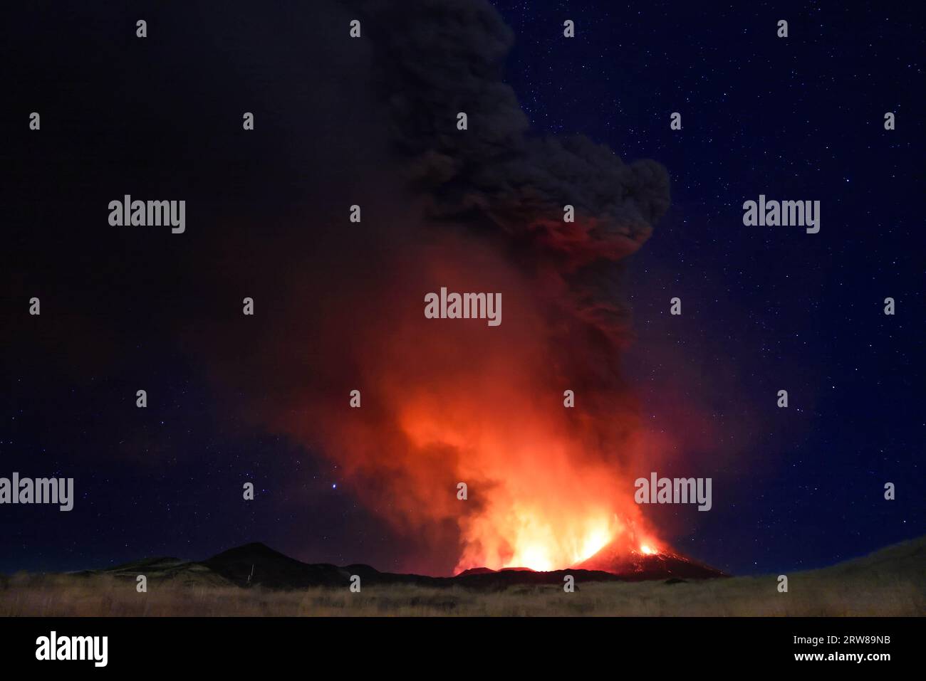 Etna eruzione in Sicilia con vista panoramica della grande colonna di fumo e cenere dal cratere vulcano nel ciel notturno stellato del agosto 2023 Foto Stock