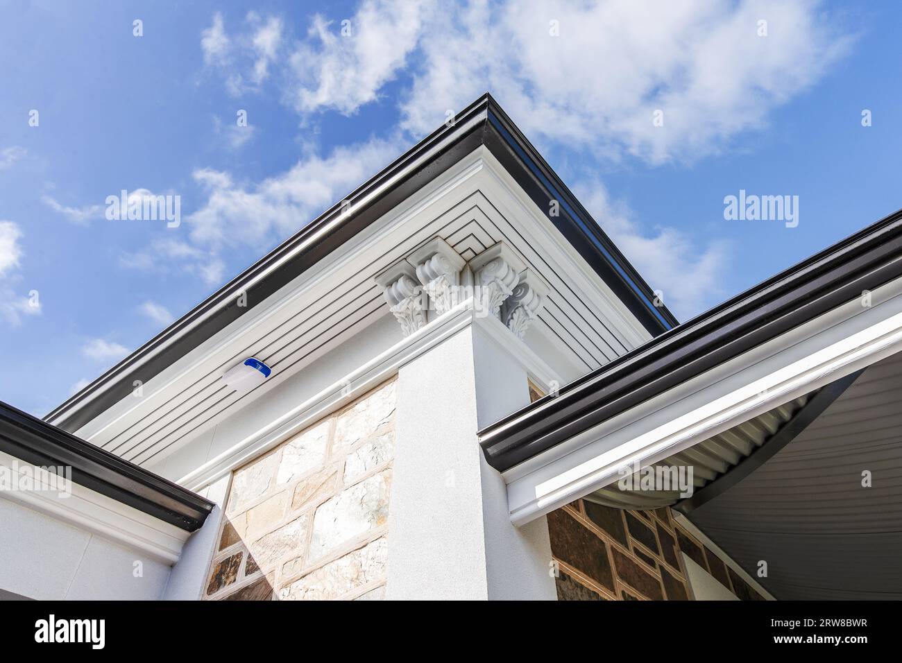 Vista ad angolo basso dell'esterno di una casa moderna caratterizzata da decorativi dettagli di cornice, pareti rese, facciata in pietra e tetti su un cielo blu Foto Stock