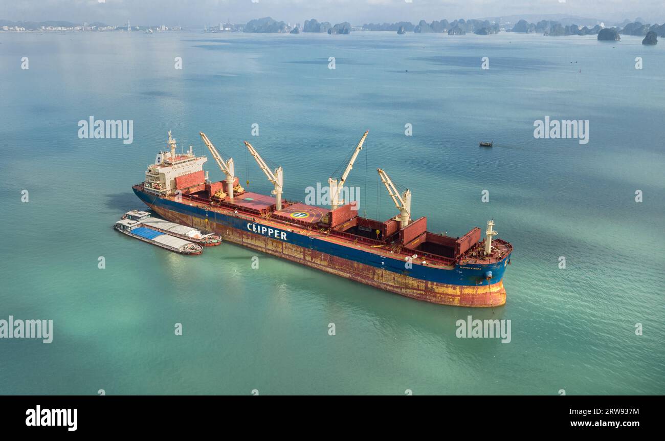 La nave portarinfuse Clipper Kythira ancorata nella baia di ha Long (Hạ Long), Vietnam, che scarica il carico in chiatte merci locali tra le scogliere calcaree turistiche Foto Stock