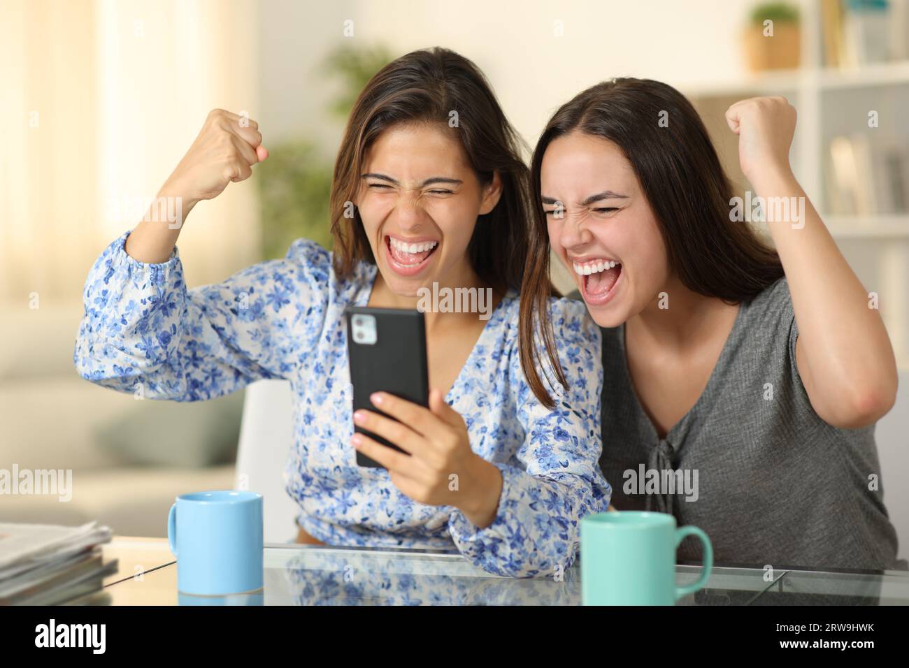 Donne entusiaste che controllano il telefono per festeggiare il successo a casa Foto Stock