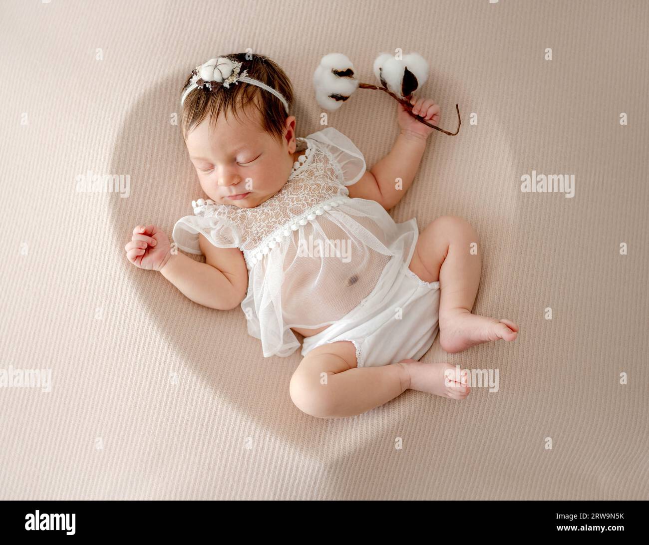 Adorabile neonata con abito bianco e corona dormendo a forma di cuore con fiore di cotone. Un bambino che sta dormendo Foto Stock