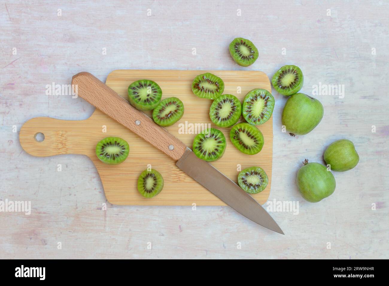 Mini kiwi, frutta intera e tagliata a metà su tavola di legno con coltello (Actinidia arguta) Foto Stock