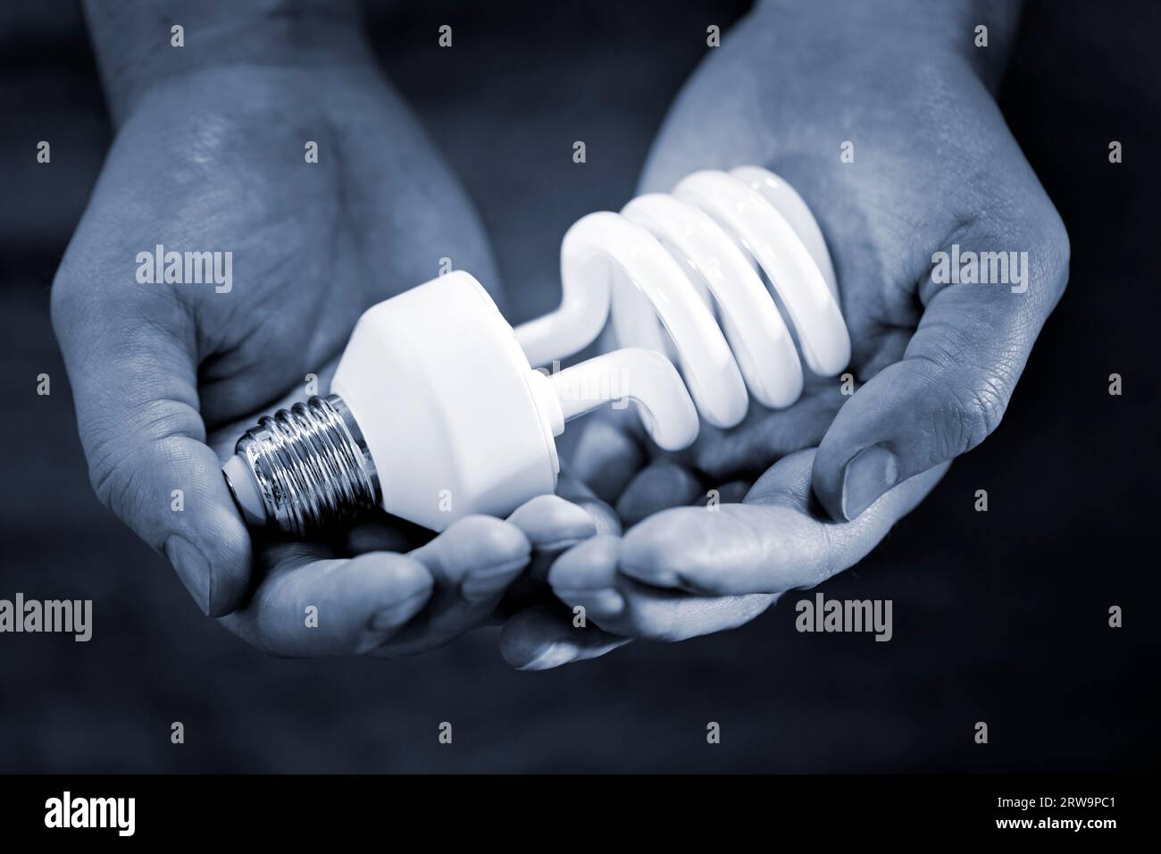 Immagine monocromatica blu delle mani con una lampadina fluorescente compatta. Profondità di campo molto breve Foto Stock