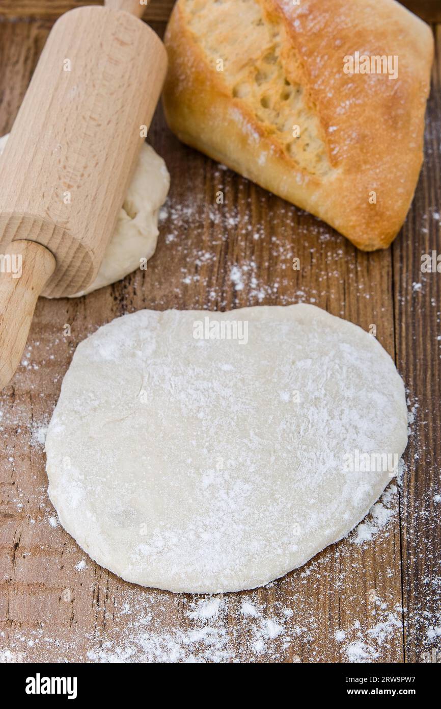 Stendere l'impasto lievitato su una tavola di legno. Dietro di esso un rotolo di impasto e un panino Foto Stock