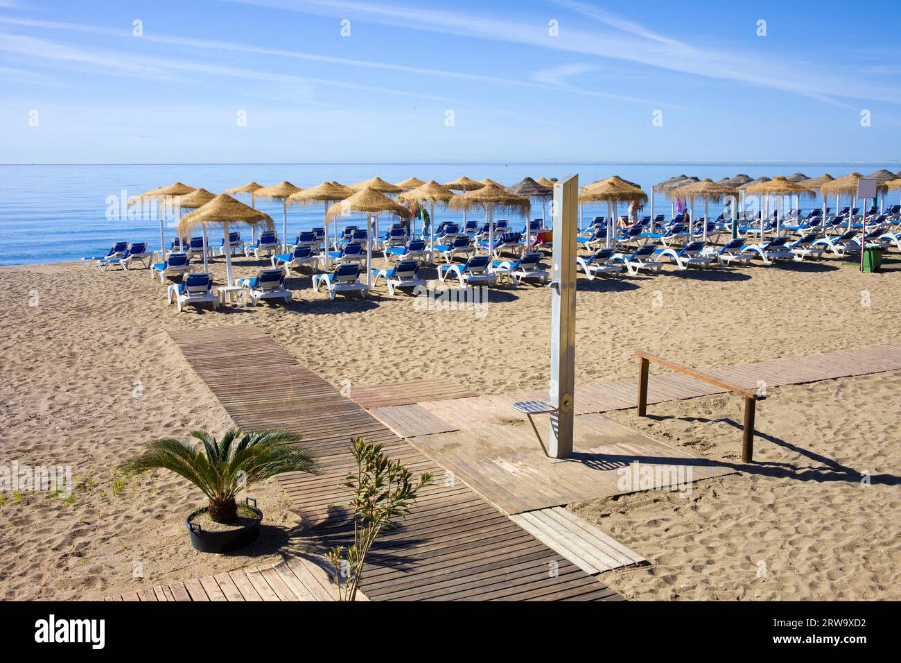 Paesaggi per vacanze estive, spiaggia di sabbia sul mare blu, sdraio, sentiero in legno e doccia nel resort Marbella sulla Costa del Sol in Spagna Foto Stock