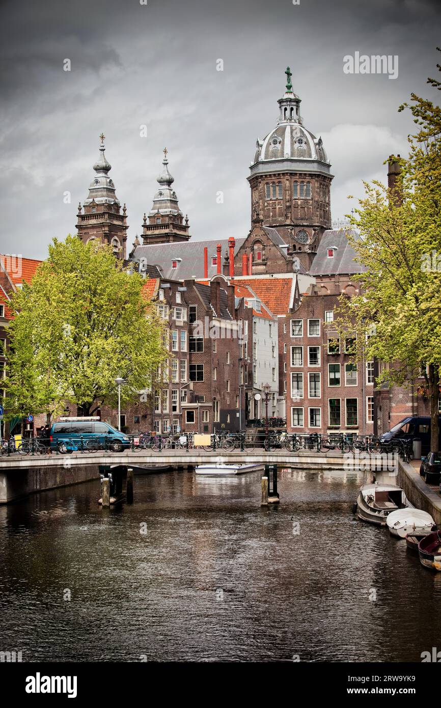 Città di Amsterdam nei Paesi Bassi, ponte, canale, edifici storici e torri della chiesa di San Nicola sullo sfondo Foto Stock