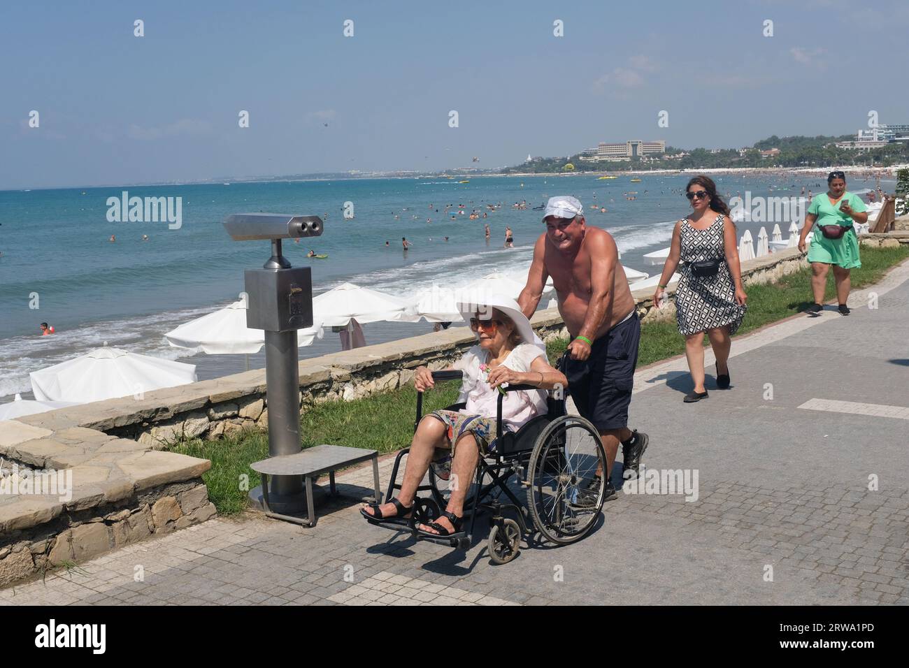 Un turista maschio che spinge la moglie su una sedia a rotelle a Side, Turchia. Foto Stock
