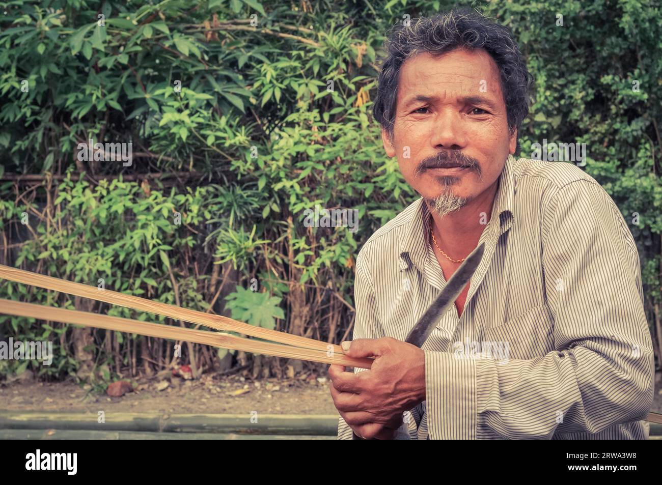 Damak, Nepal, circa maggio 2012: Vecchio inginocchiato vestito di abiti bianchi tiene il coltello nel campo profughi nepalese di Damak, Nepal. Documentario editoriale Foto Stock