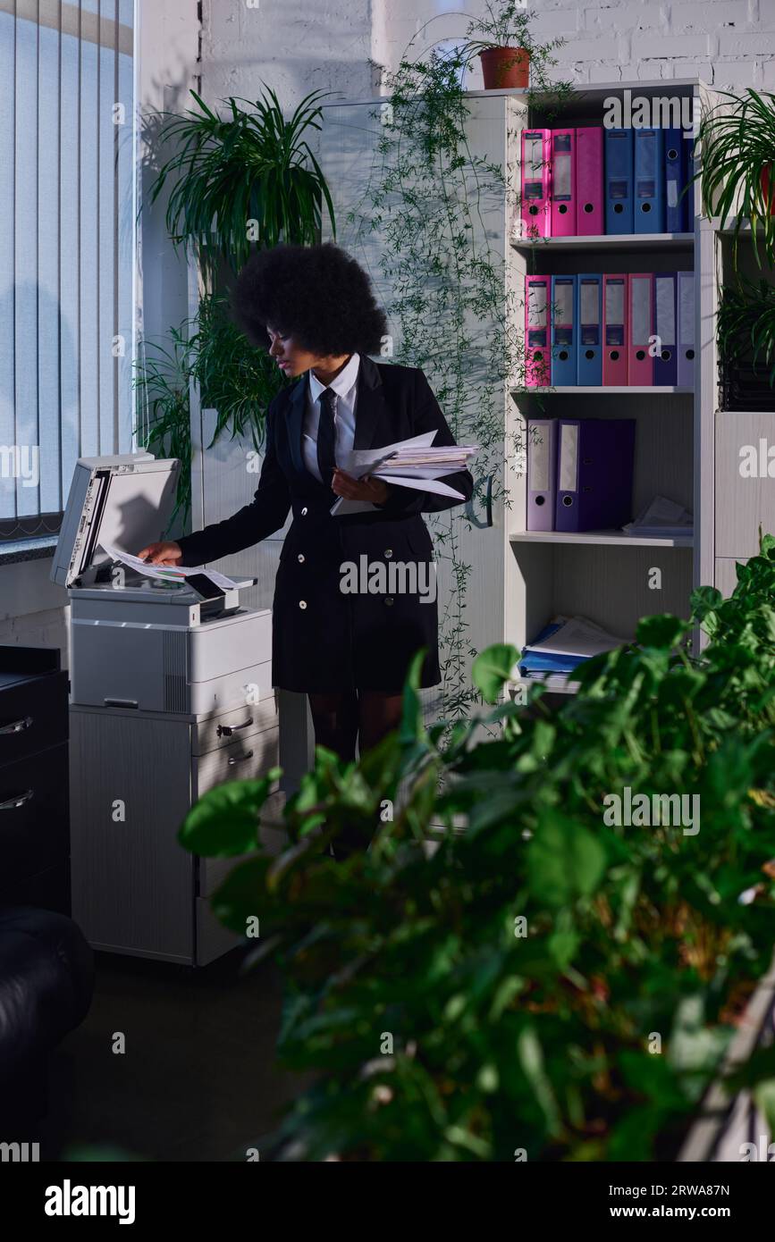 giovane donna afroamericana che copia documenti su una fotocopiatrice la sera in ufficio, lavoro eccessivo Foto Stock