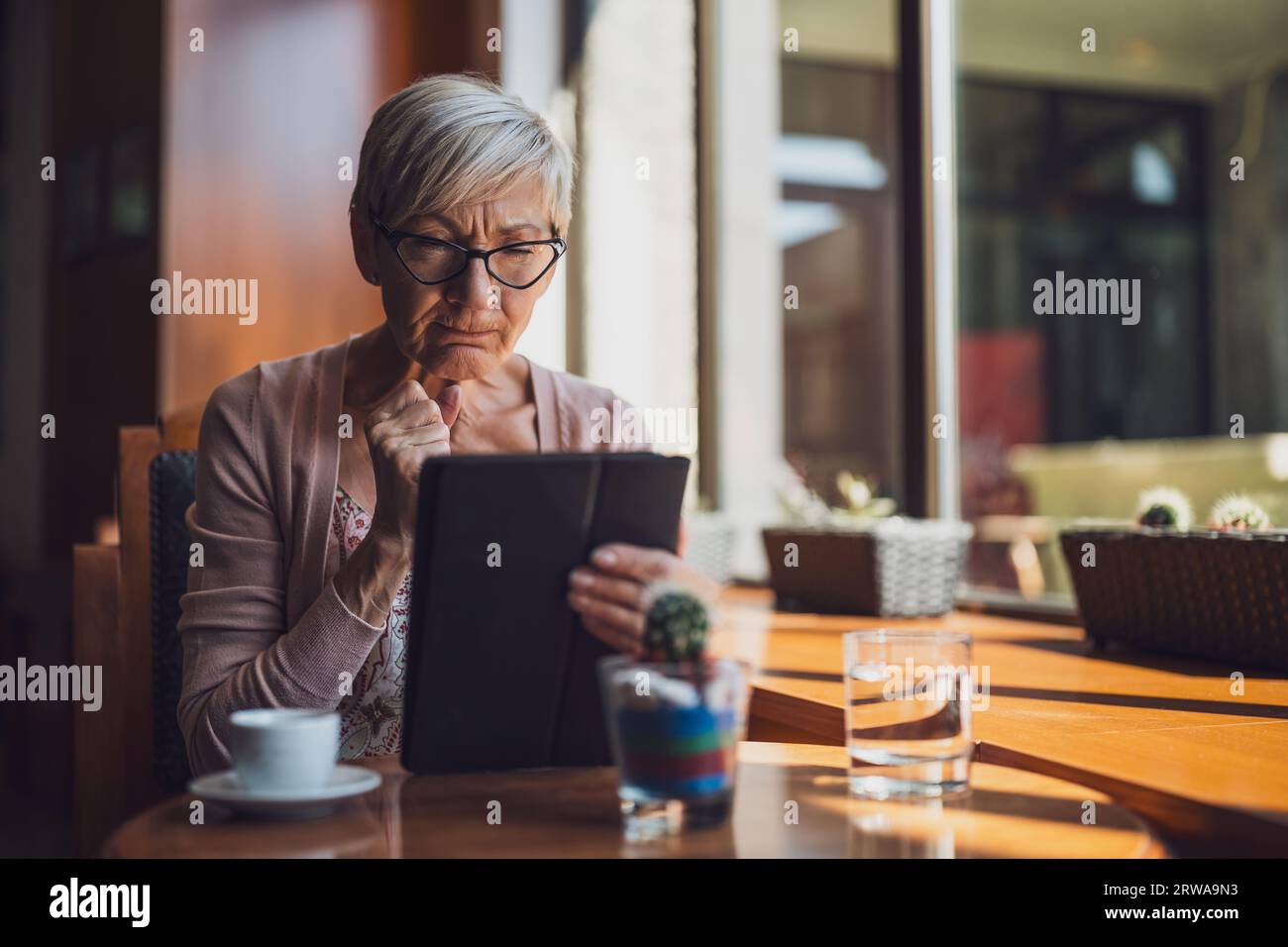 Una donna matura è seduta in una caffetteria e utilizza un tablet digitale. Foto Stock