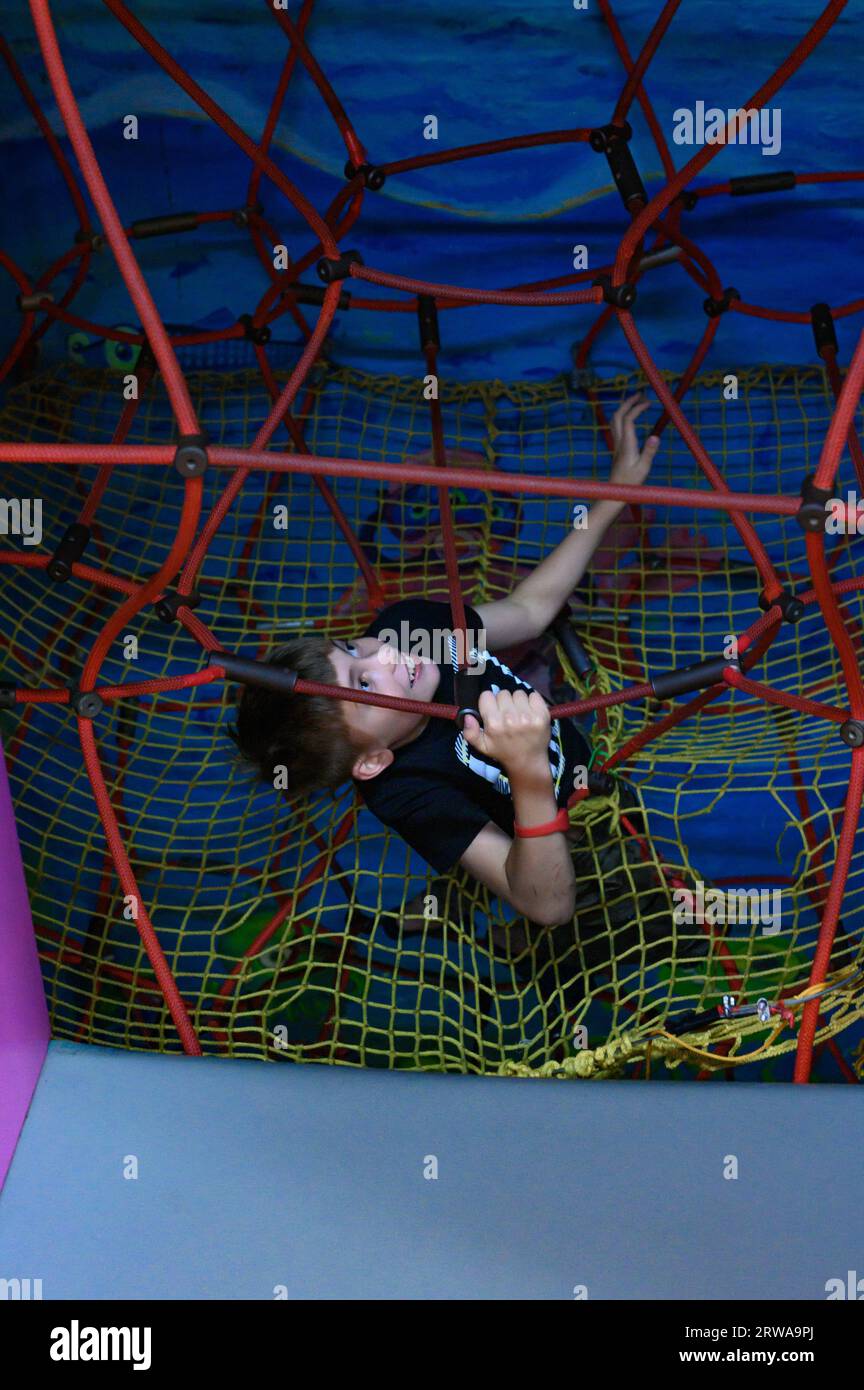 Il ragazzo sale il labirinto con una ragnatela, attività per bambini nella sala giochi. Foto Stock