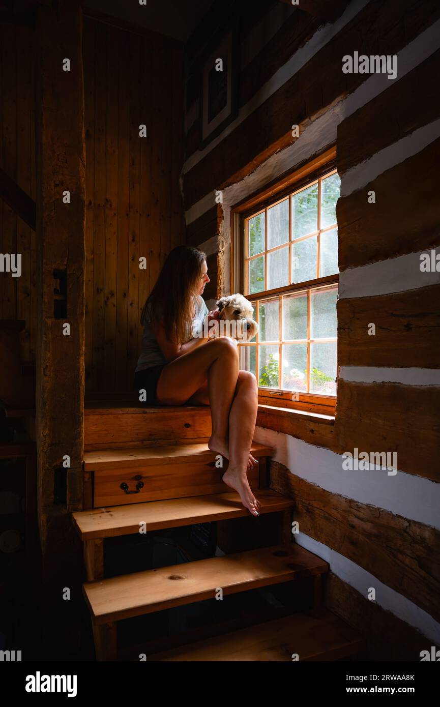 Donna e cane seduti accanto a una finestra sulle scale della casa di legno. Foto Stock