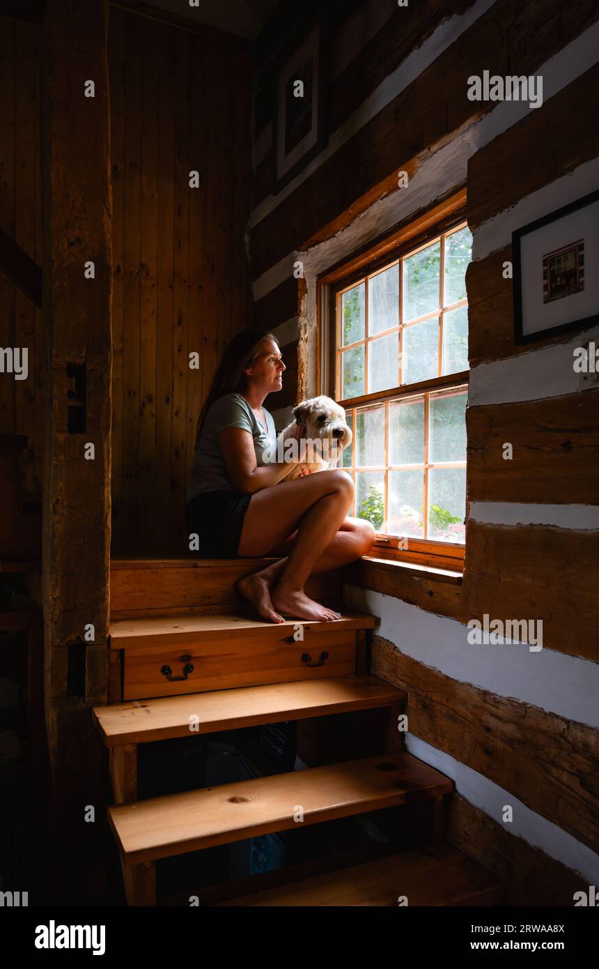 Donna e cane seduti accanto a una finestra sulle scale della casa di legno. Foto Stock